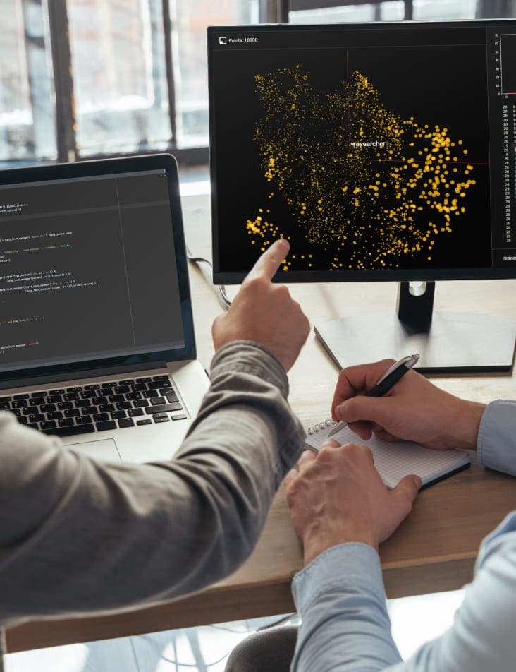 Two people collaborating at a desk and pointing at data on a computer screen