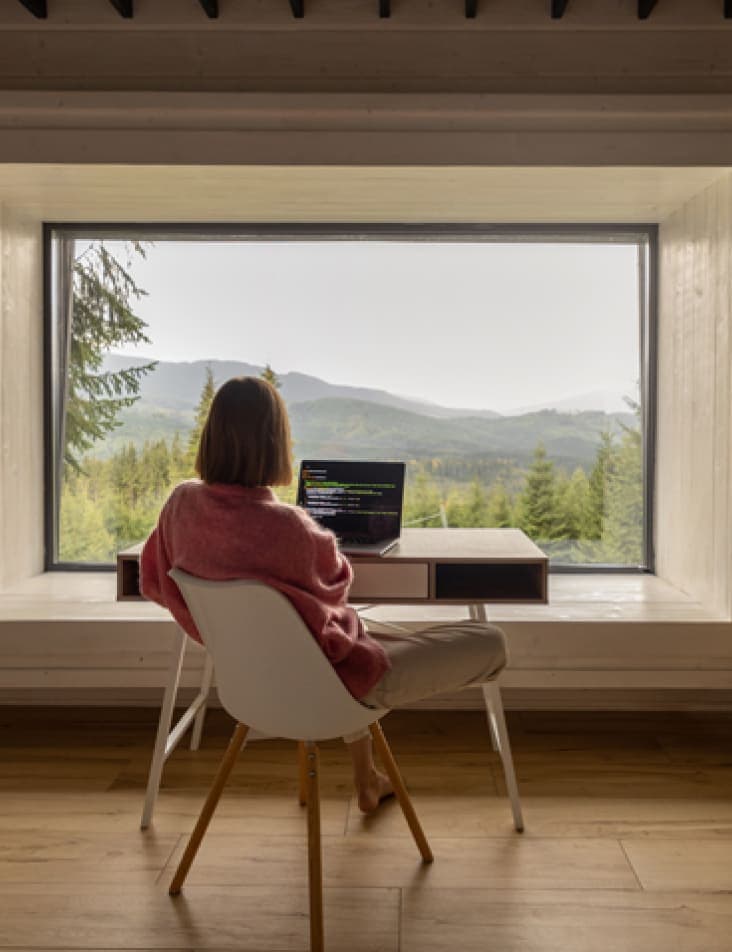 A person working on a computer in front of a window in their living room