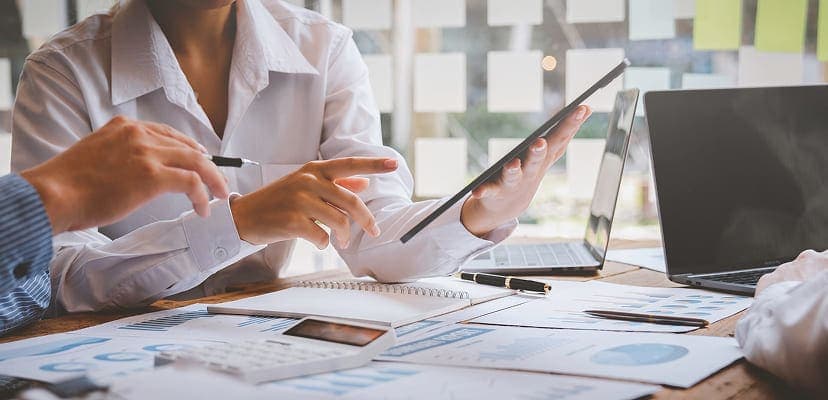 people working at desk with papers, laptops, ipads, and charts and graphs in finance industry